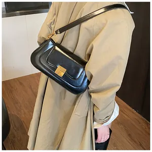 Detailansicht der schwarzen Baguette-Tasche aus Leder mit goldener Schließe am Trenchcoat