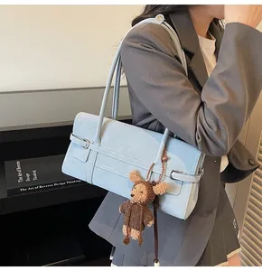 Detail of light blue shoulder bag with leather strap and brown plush bear charm