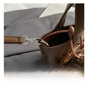 Detail of silver metal hook and brown lychee grain leather on a crossbody bucket bag