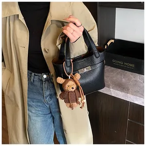 Detail of black lychee grain bucket bag with silver lock and a brown teddy bear charm