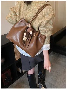 Detail of a large brown matte leather tote bag with a cute bear pendant on a model