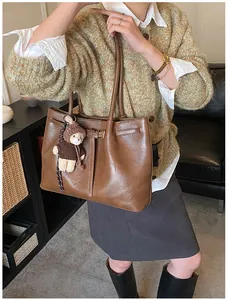 Close-up of brown leather tote bag with metallic buckle and cute teddy bear charm