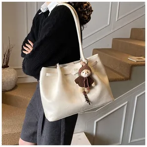 Detail of cream leather tote bag with decorative straps and a cute brown bear charm