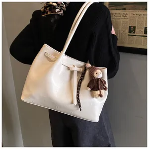 Detail of cream tote bag with cross-lace decor and brown plush bear charm on shoulder