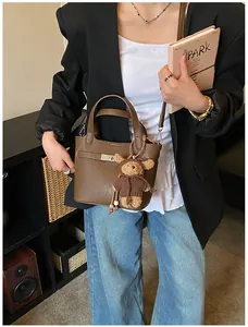Close-up of brown litchi grain leather bucket bag with metal lock and bear plush pendant