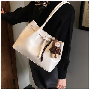 Detail of off-white tote bag with decorative knot and cute teddy bear plush charm