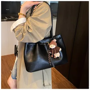 Detail of black leather tote bag featuring a side buckle and cute brown plush bear charm