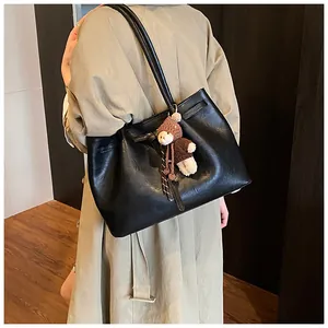 Detail of black faux leather tote bag with soft texture and cute teddy bear pendant
