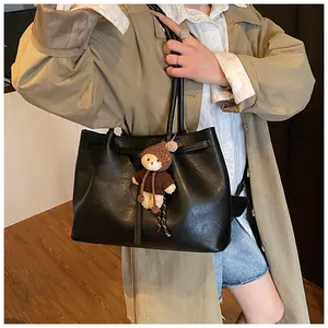 Detail of black faux leather tote bag with drawstring closure and cute bear pendant