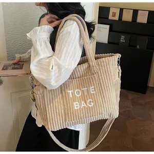 Close-up of beige corduroy tote bag featuring adjustable strap and TOTE BAG embroidery