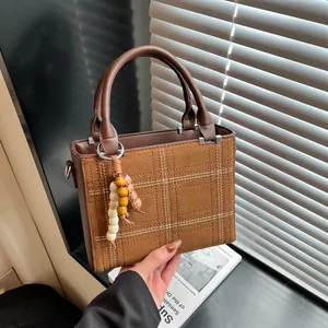 Minimalist brown suede tote bag with white quilted stitching and beaded tassel charm