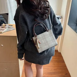 Minimalist checkered handbag with brown leather trim and beaded charm on grey sweater