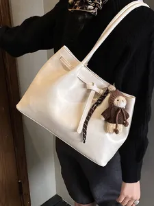 Cream white leather tote bag with bow detail and cute bear charm shown on shoulder