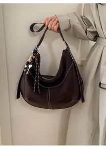 Détail d'un sac hobo marron foncé avec coutures contrastées et breloque à pompon en cuir