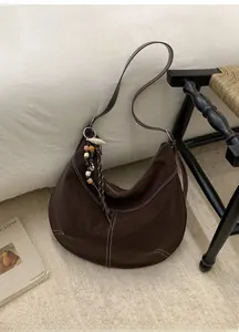 Détail du sac hobo café foncé avec coutures blanches contrastées et pendentif ethnique