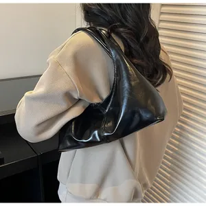 Detail of a black patent leather hobo bag with a glossy finish on a model's shoulder