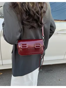 Detail of dark red baguette bag with glossy finish and tassel accents on model