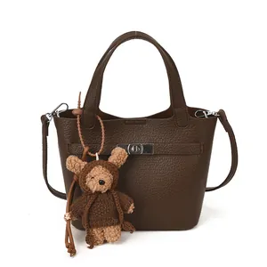 Brown bucket bag in litchi leather texture with a cute plush bear charm and silver clasp
