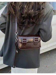 Detail of dark brown glossy leather crossbody bag with decorative buckles and silver knots