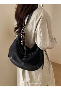 Détail du sac demi-lune en cuir noir avec surpiqûres blanches et pendentif perlé rétro