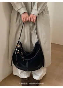 Détail du sac fourre-tout noir en demi-lune avec surpiqûres blanches et pendentifs