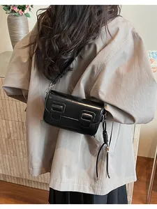 Detail of a black glossy baguette bag with decorative buckles and fringe on a model