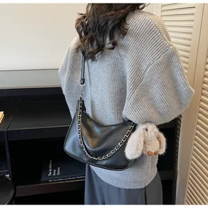 Detail of black faux leather baguette bag with metal chain and plush bunny charm
