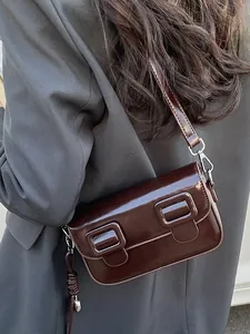 Minimalist dark brown patent leather baguette bag with dual square buckles on a model