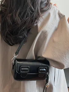 Minimalist black baguette shoulder bag with silver heart charm on a model's shoulder