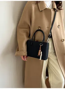Detail of black textured crossbody bag with wooden bead charm on a camel coat outfit