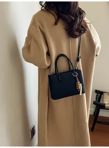 Detail view of black textured mini tote bag with beaded charm on camel wool coat