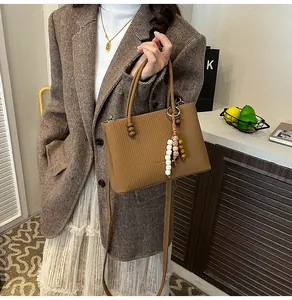 Detail of a brown ribbed crossbody bag with wooden beads and a colorful charm