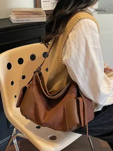 Sac hobo en daim marron avec garniture en cuir, porté comme sac à bandoulière chic
