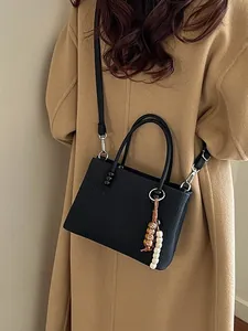 Chic black textured square handbag with beaded charm shown on model in tan coat