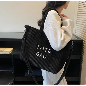 Detail of black corduroy tote bag showing embroidered text and adjustable shoulder strap