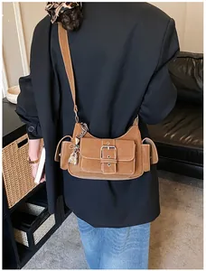 Détail du sac baguette en daim marron avec poches fonctionnelles et pendentif cadenas argent