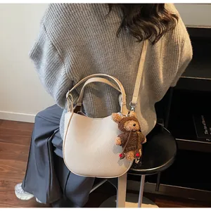 Detail view of cream white textured leather bucket bag with cute bear charm on shoulder