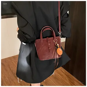 Détail du sac seau vintage rouge-brun avec un pendentif smiley en peluche orange