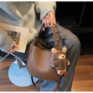 Detail of a dark brown pebble leather bucket bag with a cute plush bear charm on the side