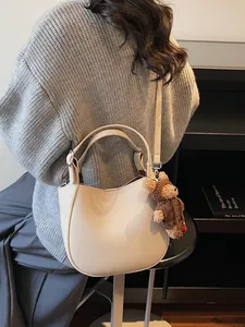 Minimalist beige pebble leather bucket bag with cute bear charm shown on a model