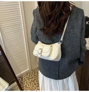 Detail of a creamy white patent leather crossbody bag with silver buckle on a model back