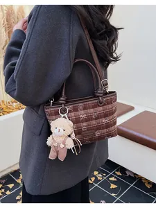 Sac seau à carreaux marron avec pendentif ours porté par un mannequin en décor d'automne