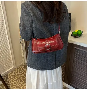 Close-up of a burgundy patent leather shoulder bag with silver buckle on a model