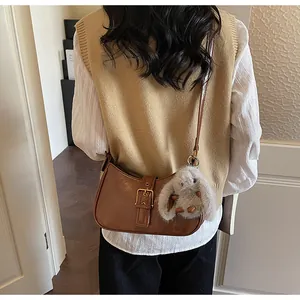 Detail view of a dark brown crescent bag with buckle and plush rabbit charm