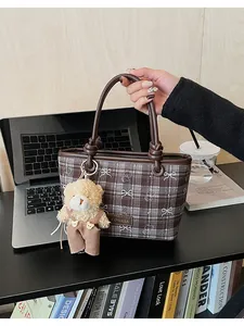 Détail du sac à main à carreaux marron avec charm ours dans un bureau moderne