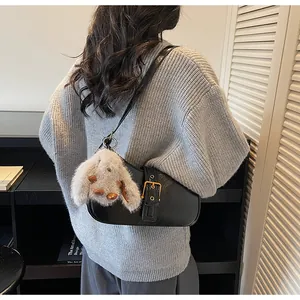 Detail of black glossy baguette bag featuring a gold buckle and cute plush bunny charm