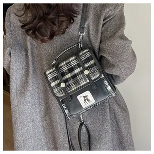 Détail d'un sac bandoulière à carreaux avec écusson d'ours et poignée en chaîne