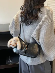 Black wrinkled baguette bag with gold buckle and plush bunny charm worn by model