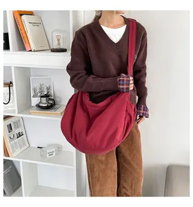 Détail du sac bandoulière en toile bordeaux avec plis à cordon porté à l'épaule
