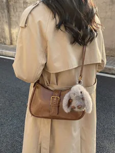 Brown vintage baguette bag with gold buckle and plush rabbit charm on a trench coat model
